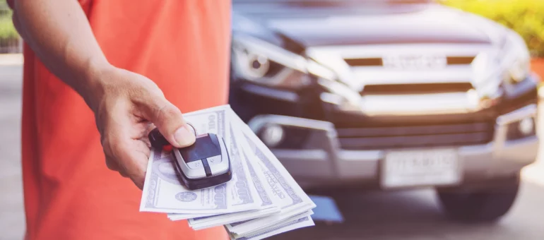 Hand holding car keys and cash in front of a car to show how to find the value of a car
